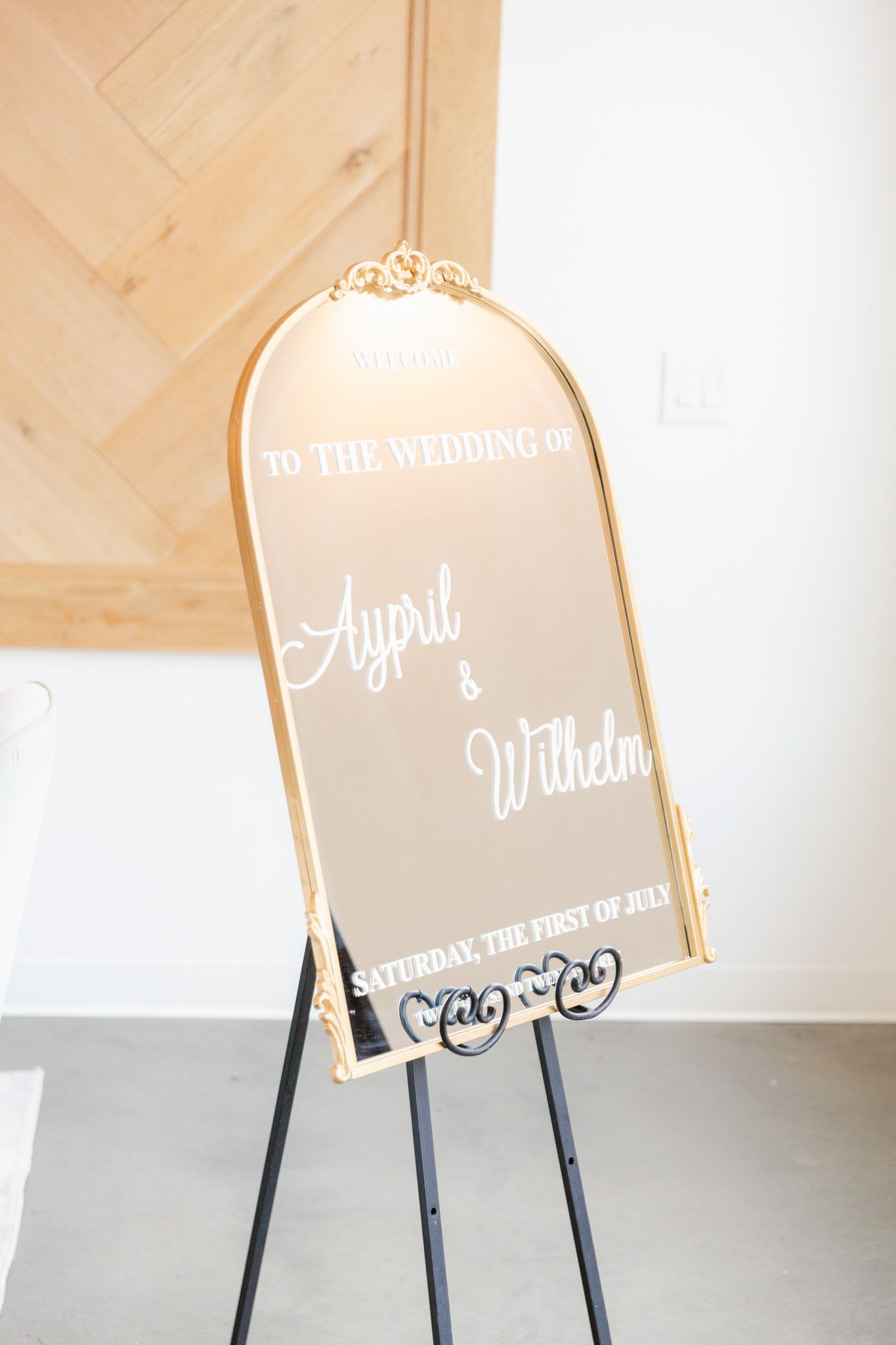 Elegant gold-framed mirror wedding welcome sign on black easel with ornate calligraphy text.