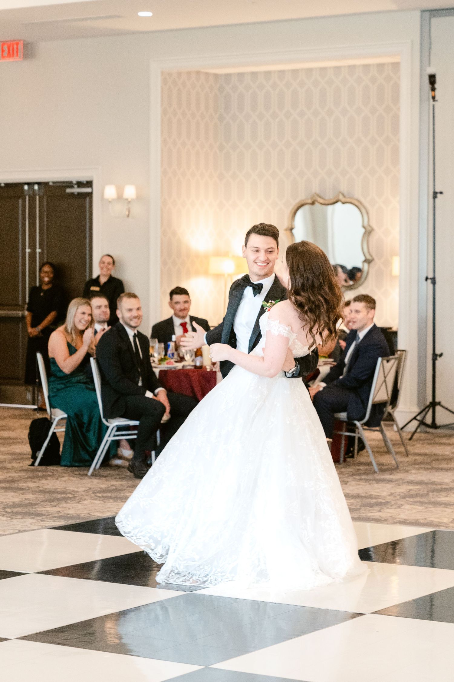 Wedding party dances and celebrates in an elegant ballroom with black and white checkered floor.