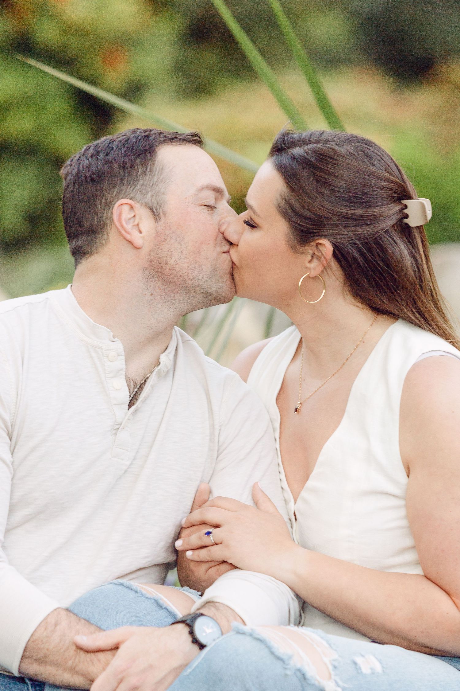 A romantic couple sharing tender kisses while sitting outdoors in casual white attire.