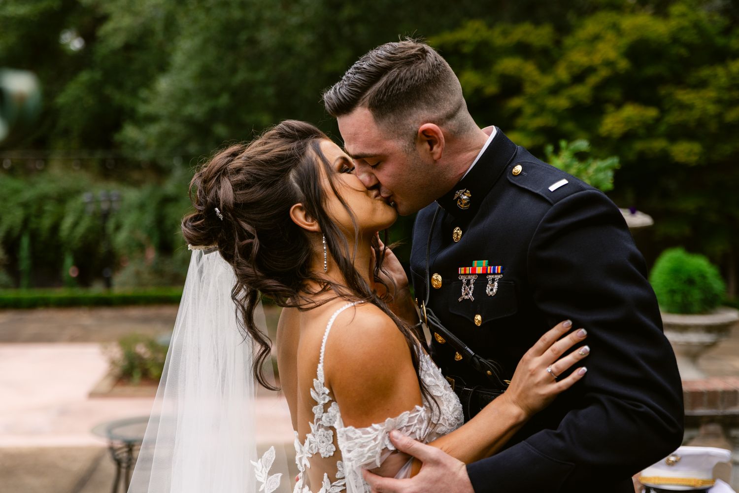 A newlywed couple shares romantic moments in an outdoor garden setting during their wedding celebration.
