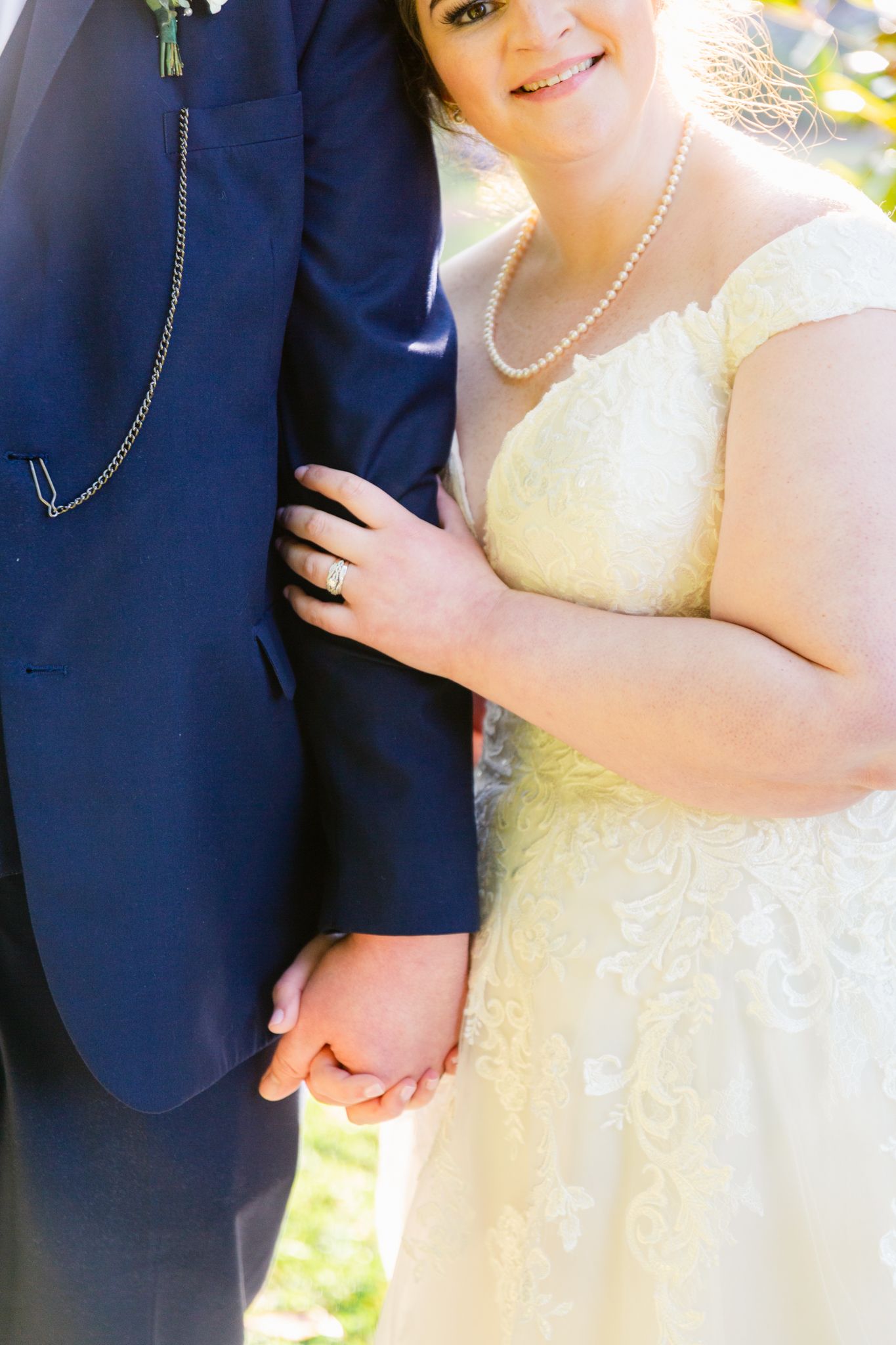 Close-up detail shots of a couple in wedding attire showing navy suit sleeve and pale yellow dress with pearl necklace.