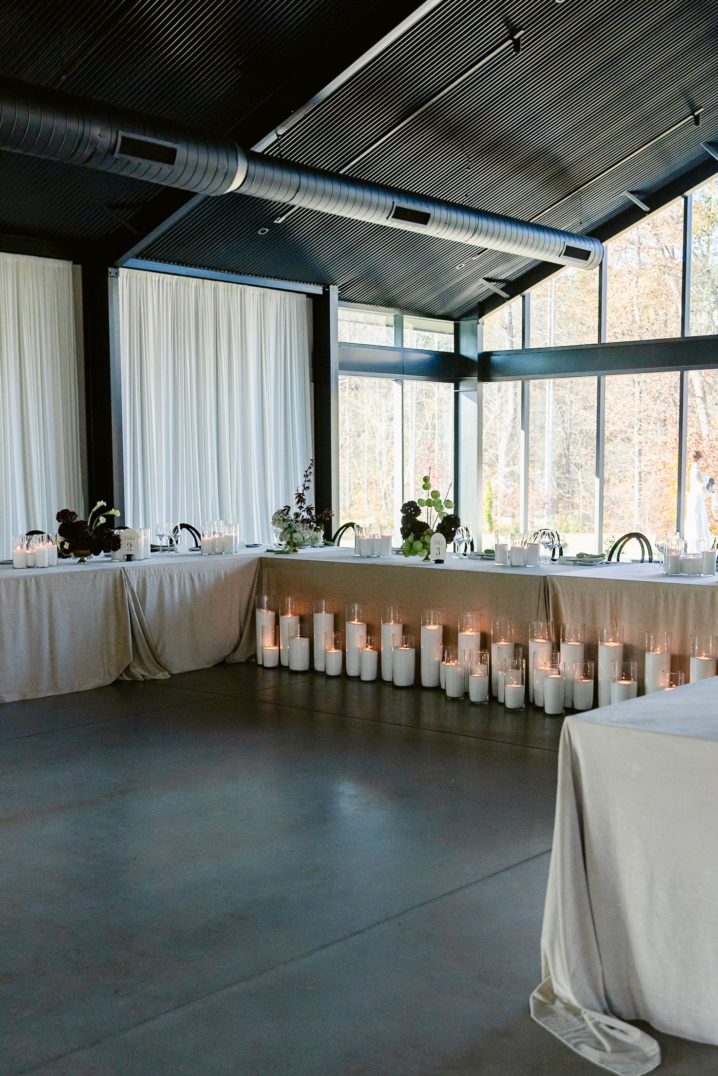 Modern event space with white drapes, long tables, and industrial ceiling details.