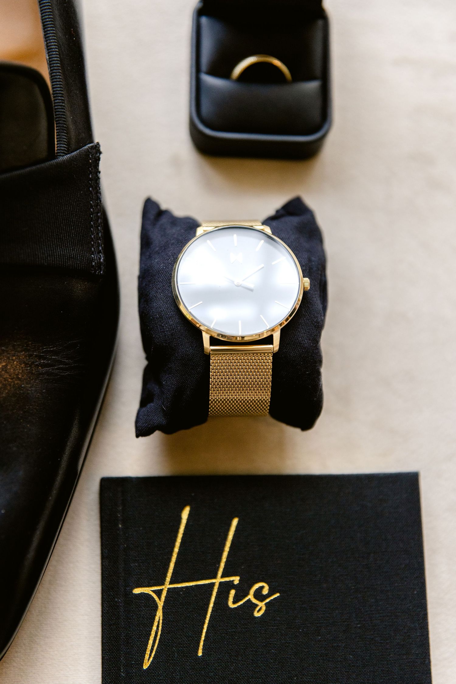 Gold mesh band watch with minimalist white face displayed on black box with elegant gold lettering.