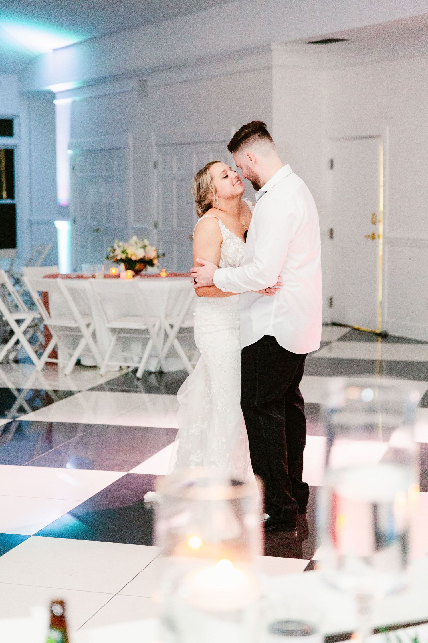 A romantic couple shares an intimate dance on a bright white dance floor with elegant decor in the background.
