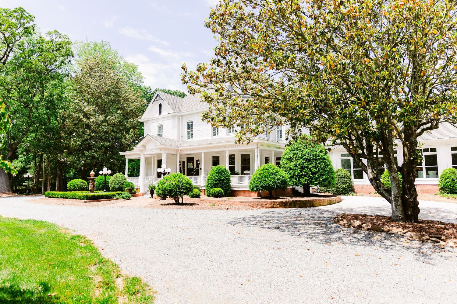 Panoramic view of a white colonial-style house with manicured lawn and landscaping.