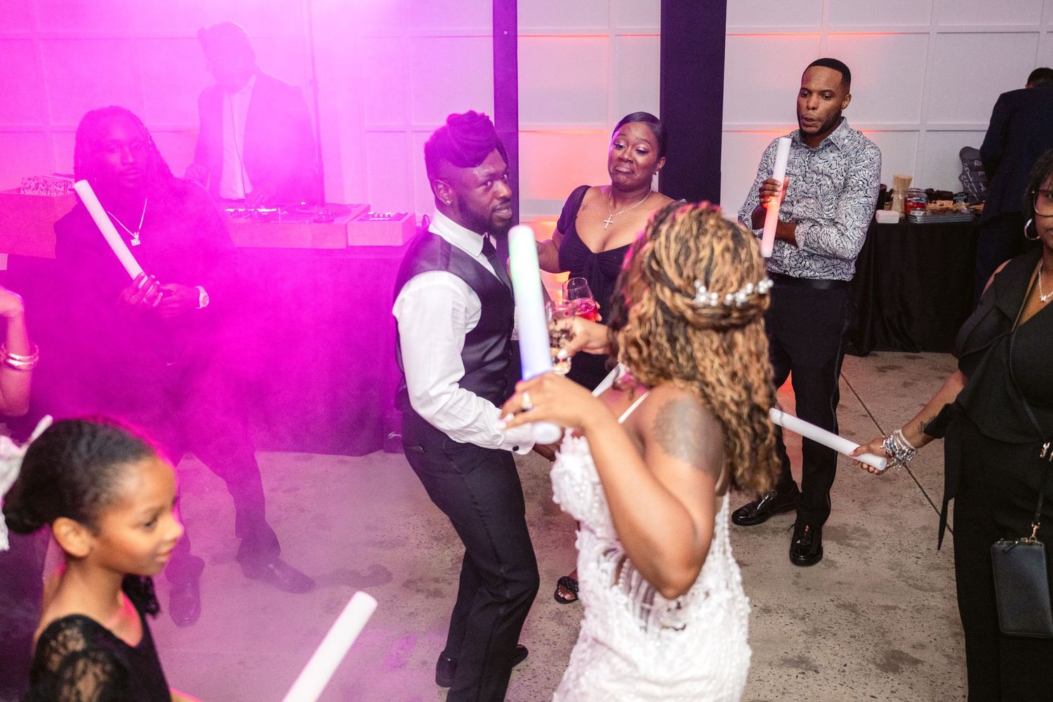 Wedding guests dancing and celebrating on the dance floor illuminated by vibrant pink lighting at a reception party.