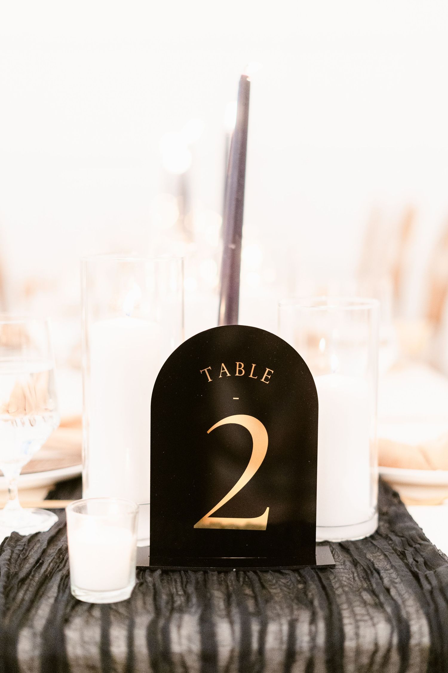 Black table number 2 sign with gold lettering displayed on a wooden surface with candles in the background.