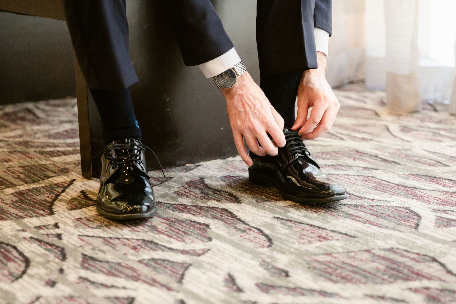 A series of black dress shoes walking on a decorative stone or tile floor pattern.