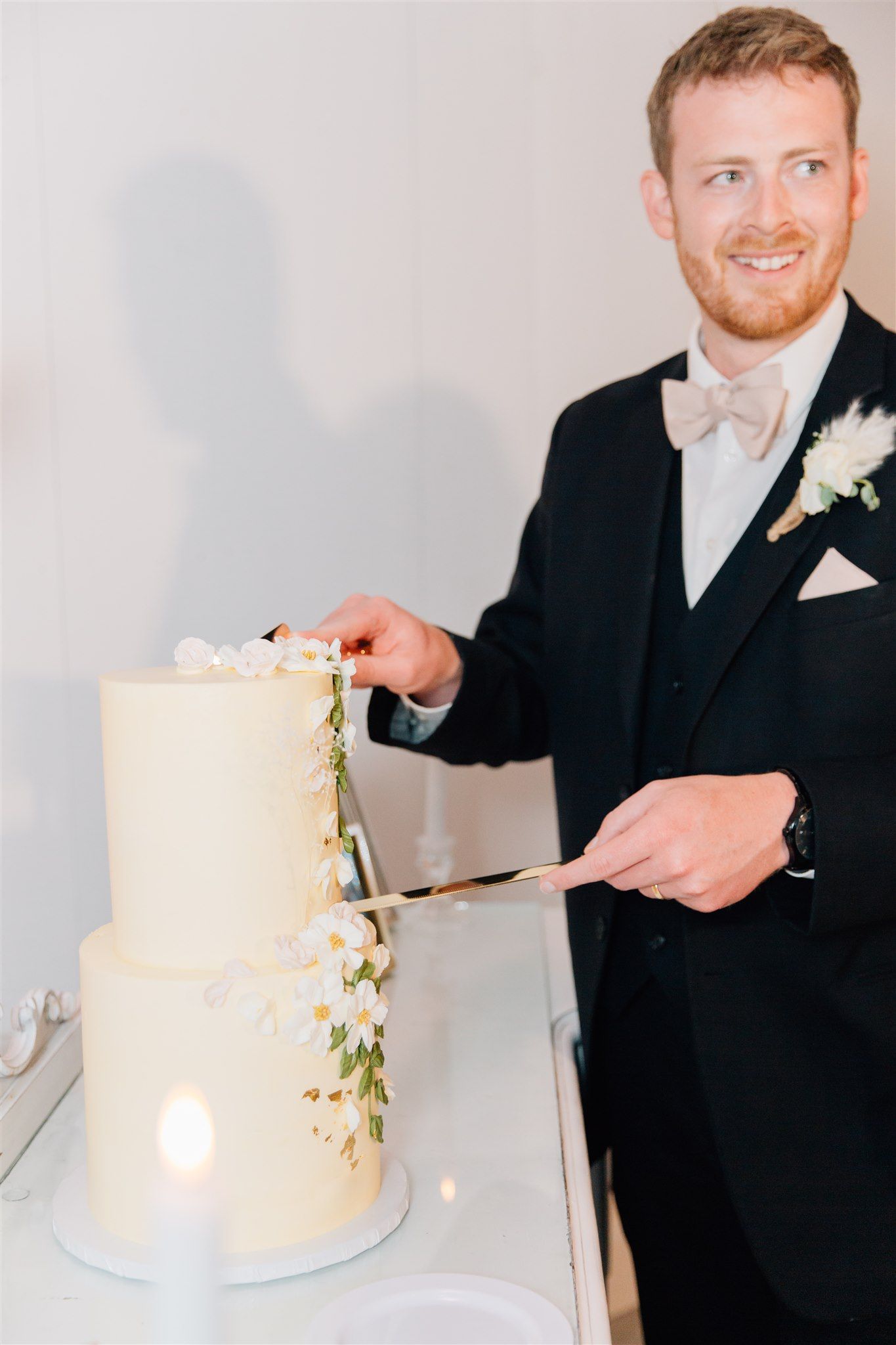 Groom in classic black tuxedo cuts elegant white two-tier wedding cake.