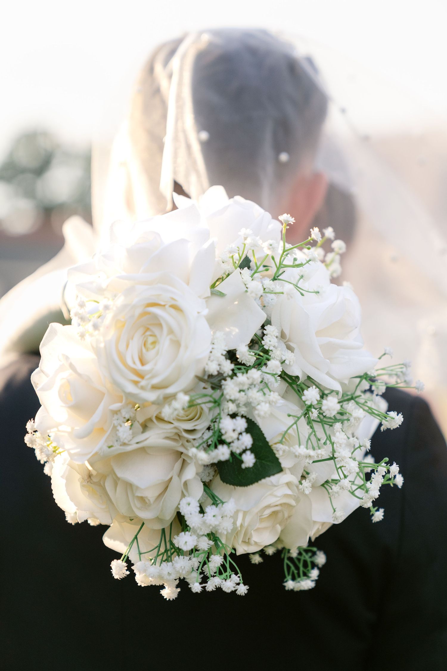 A romantic white rose bridal bouquet with baby's breath flowers photographed in soft sunlight.