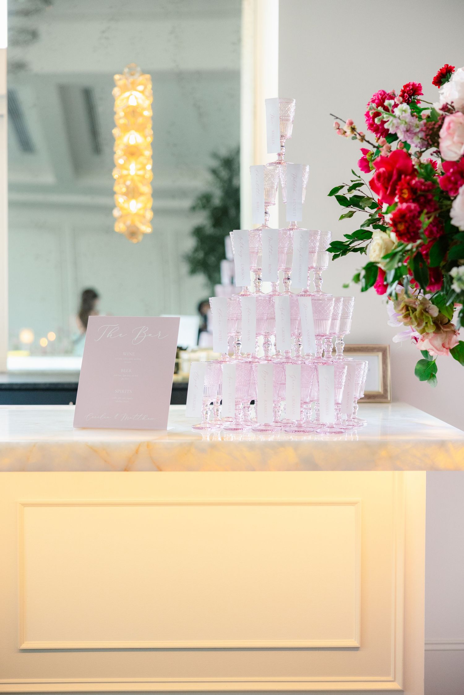Wedding reception bar setup with pink candles and red floral arrangements.