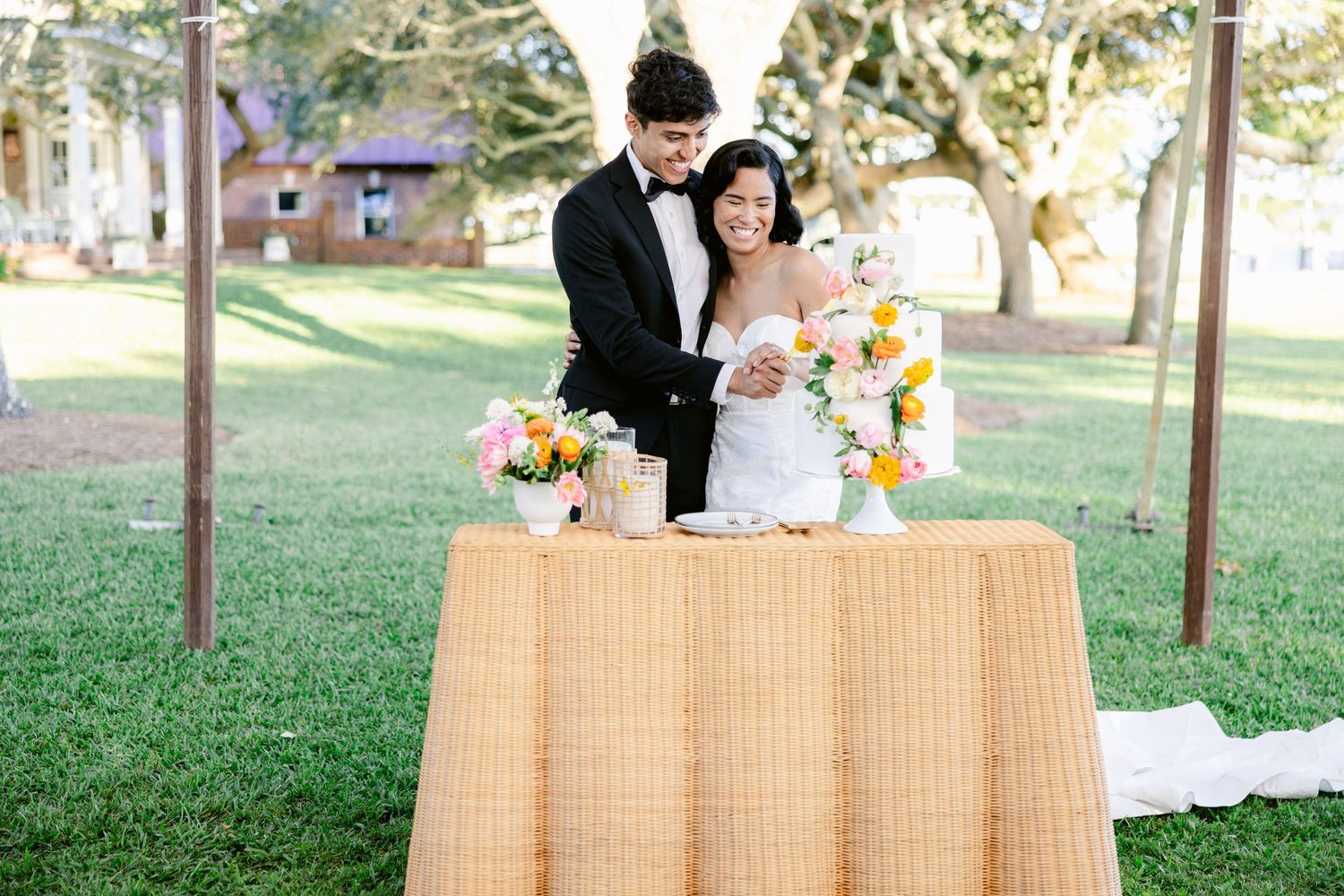 A couple stands behind their wedding cake table at an outdoor reception.