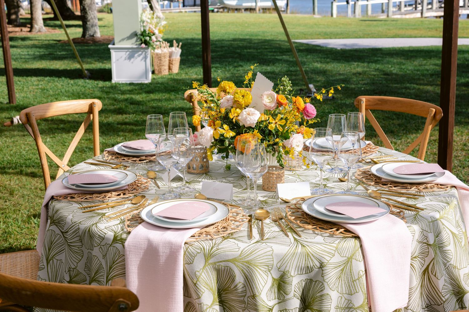 Romantic garden wedding table setting with yellow floral centerpiece and pink napkins on patterned tablecloth.
