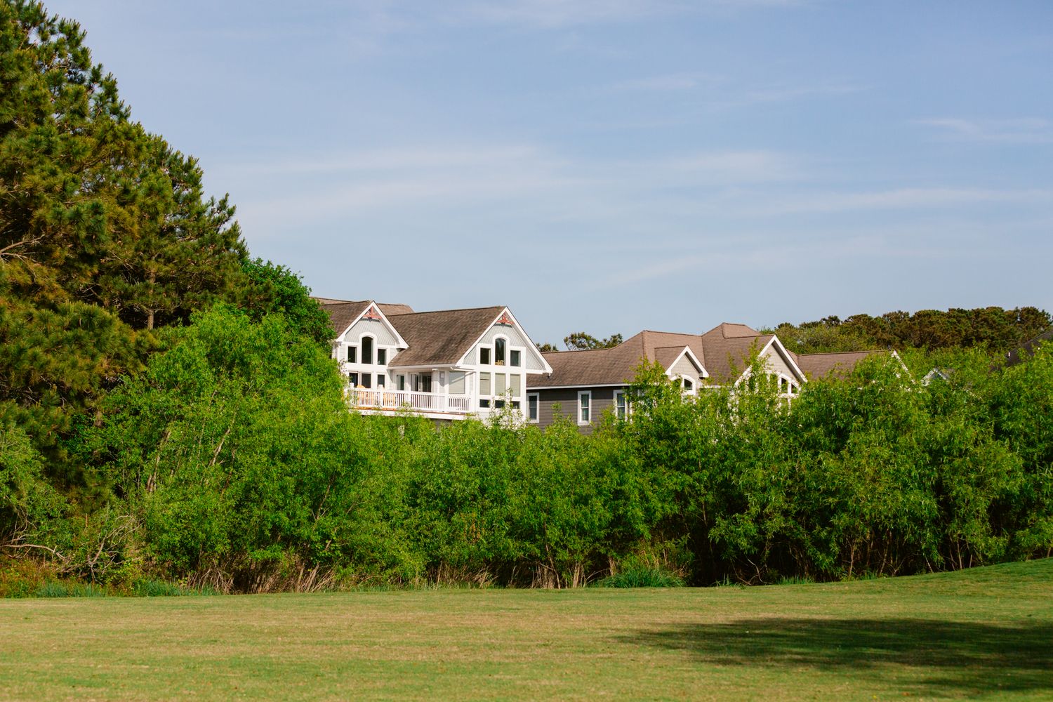 A panoramic view of a lush green golf course with residential homes visible along the treeline in the background.