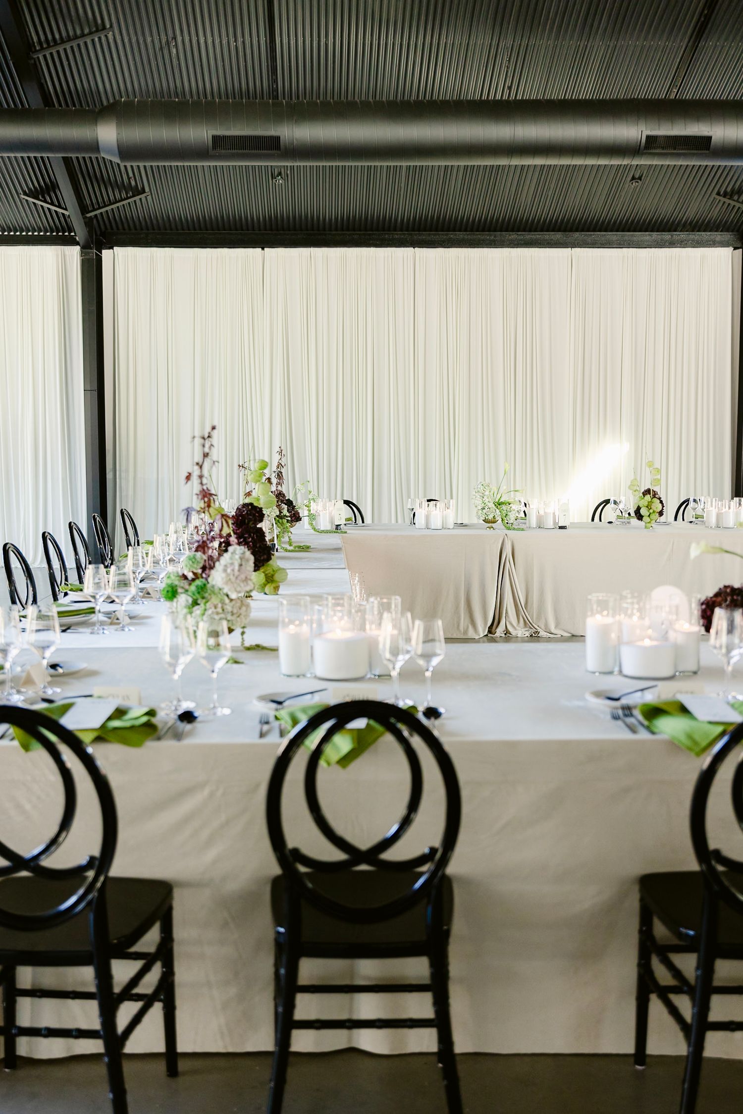 Elegant wedding reception table setup with white linens and black chairs in an industrial-style venue.