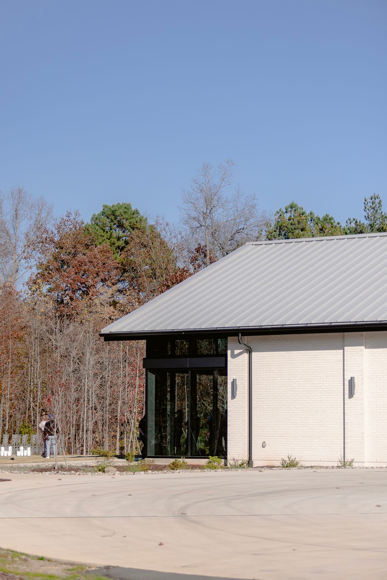 Modern white commercial building with metal roof and large windows set against a wooded background.