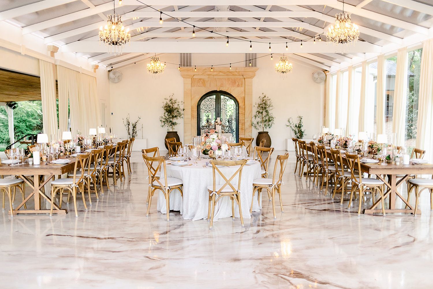 A bright, airy wedding reception venue with white decor, exposed beams, and elegant chandeliers in a rustic-chic style.