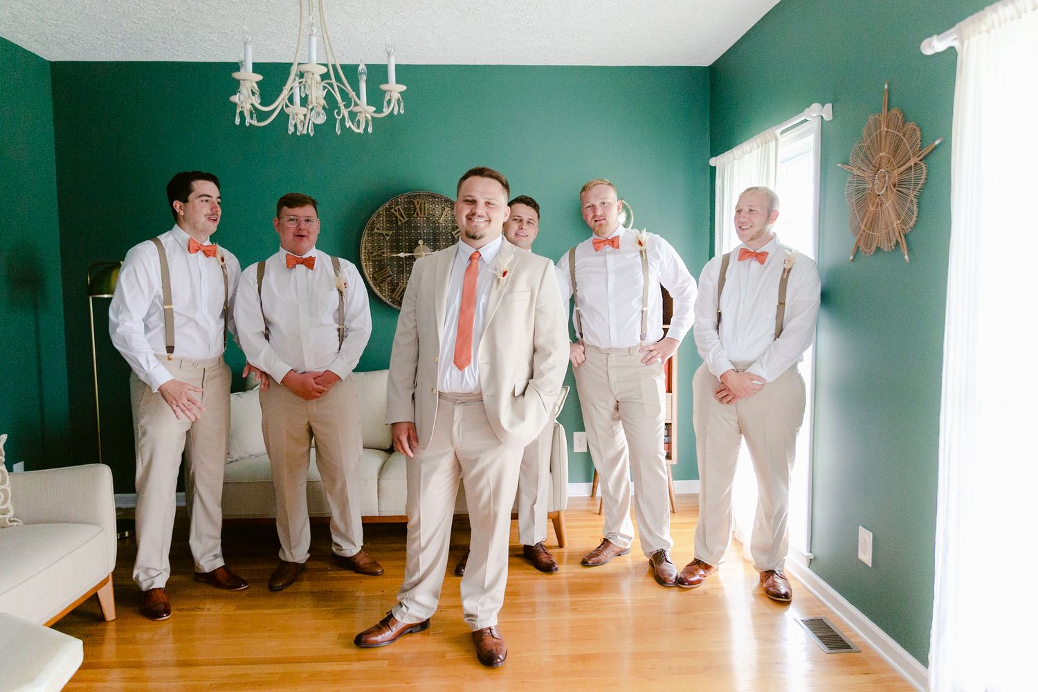 Wedding party members in white and khaki attire pose against emerald green walls in an elegant room.