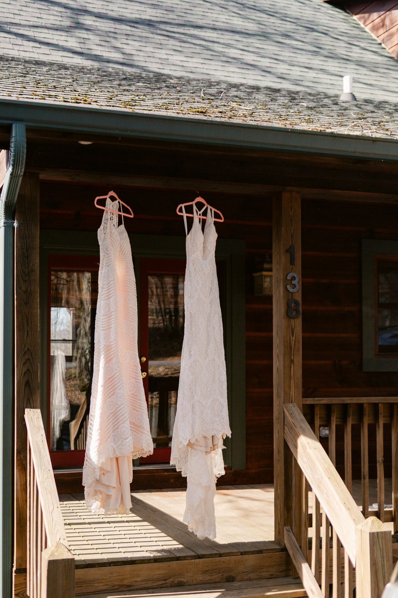 White wedding dresses hanging on wooden railings of a rustic cabin porch in natural daylight.
