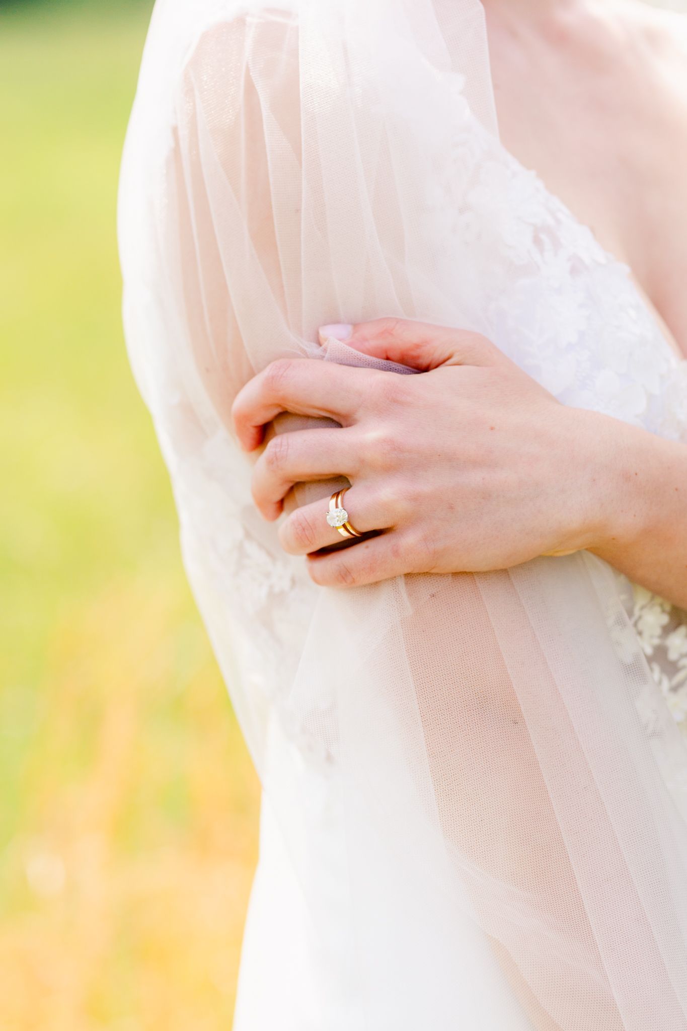 A delicate hand wearing a wedding ring rests against soft white lace fabric in golden sunlight.