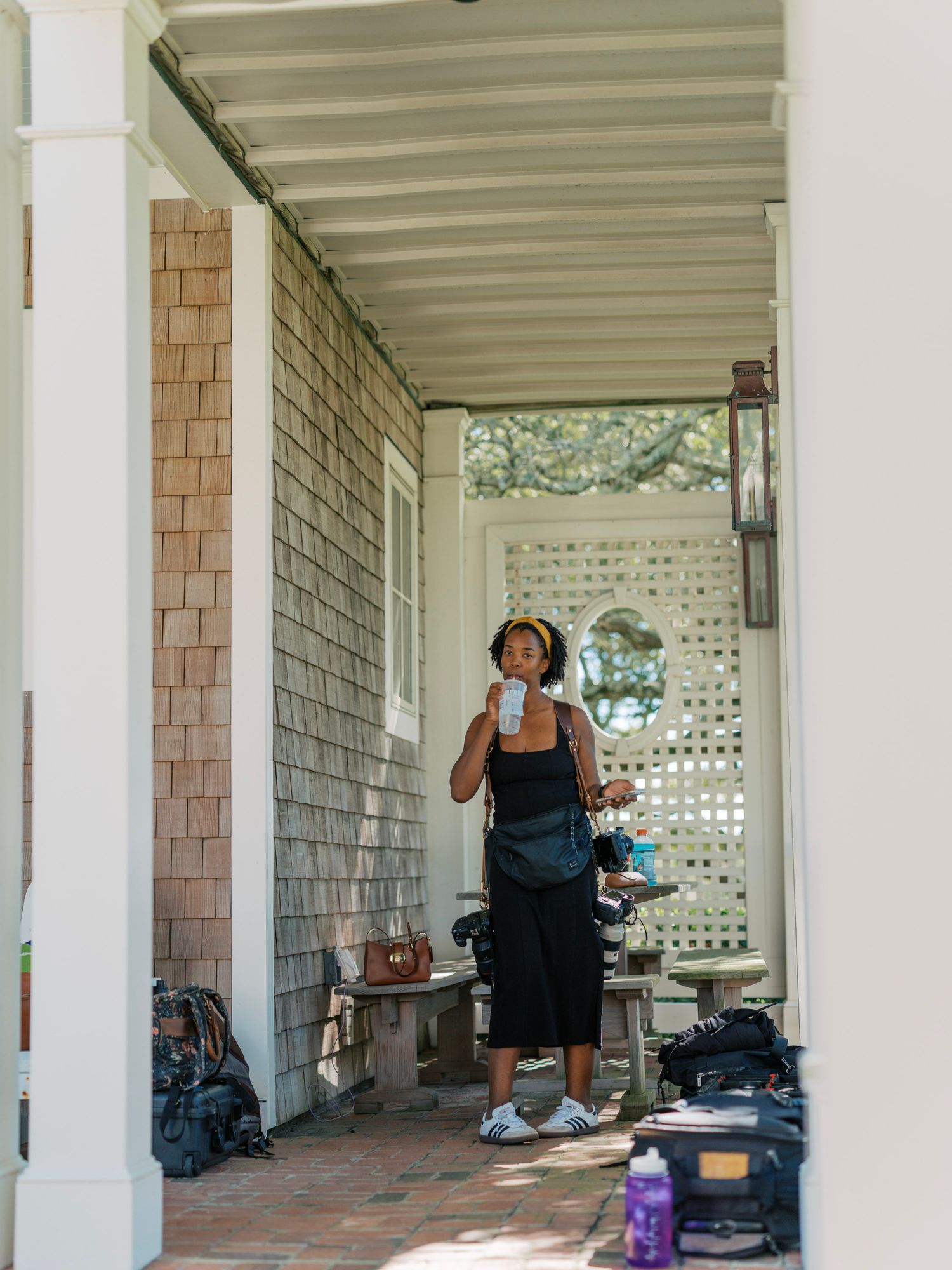 Person in a black tank top practicing yoga poses on a covered porch with white columns and shingle siding.