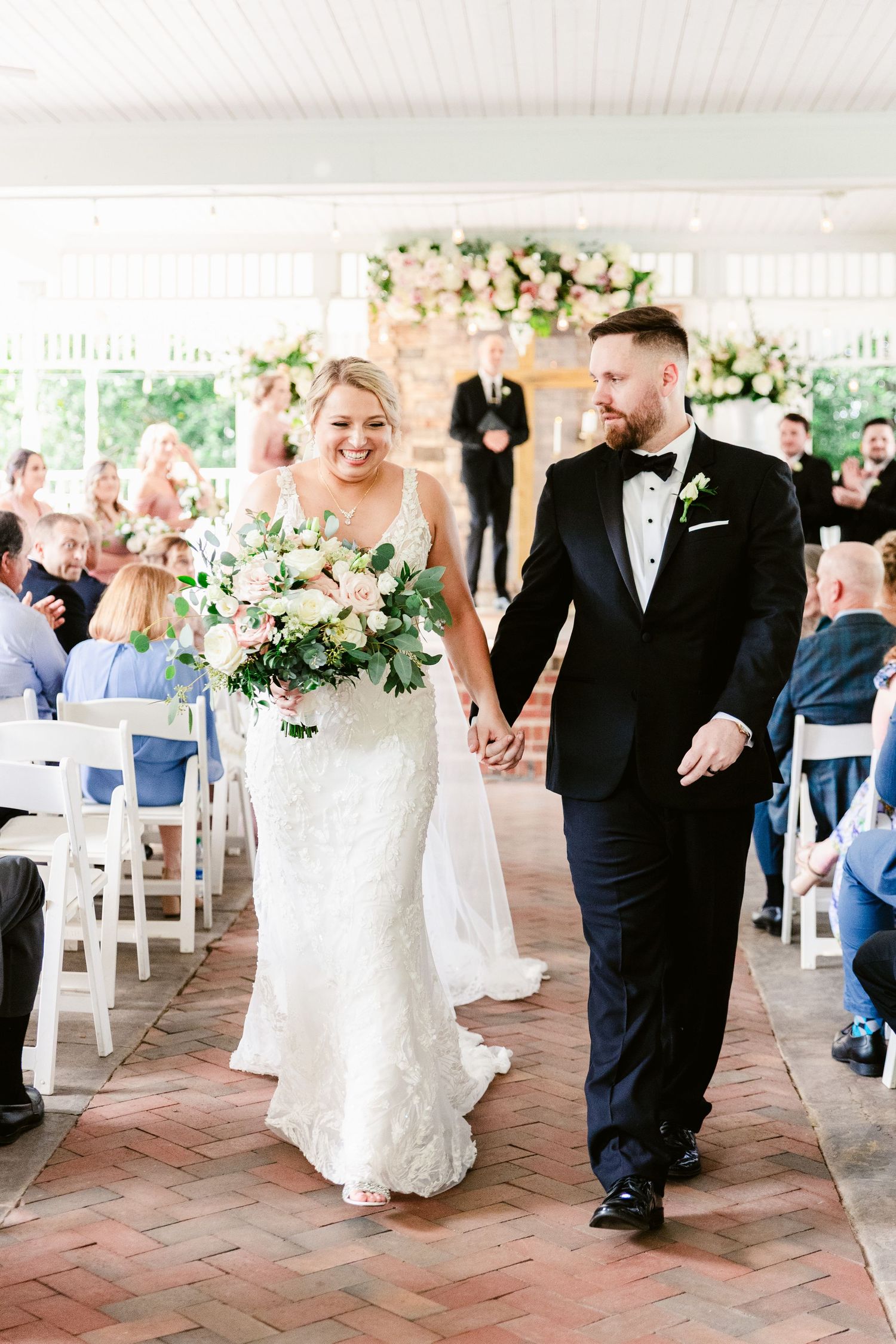 Wedding couple shares their first dance on a brick patio surrounded by guests and white floral arrangements.