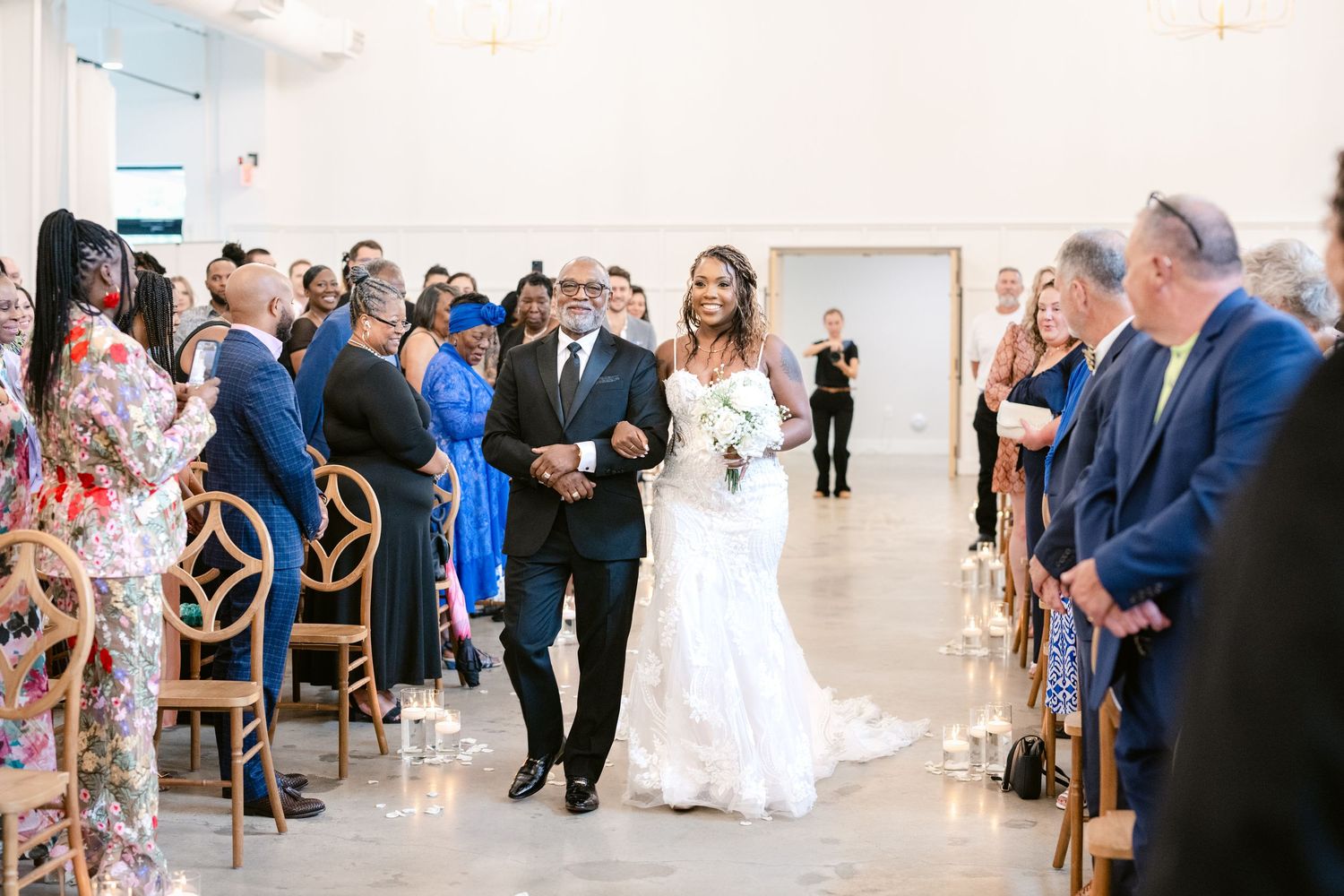 Wedding ceremony in progress in an elegant white venue with guests seated in rows.