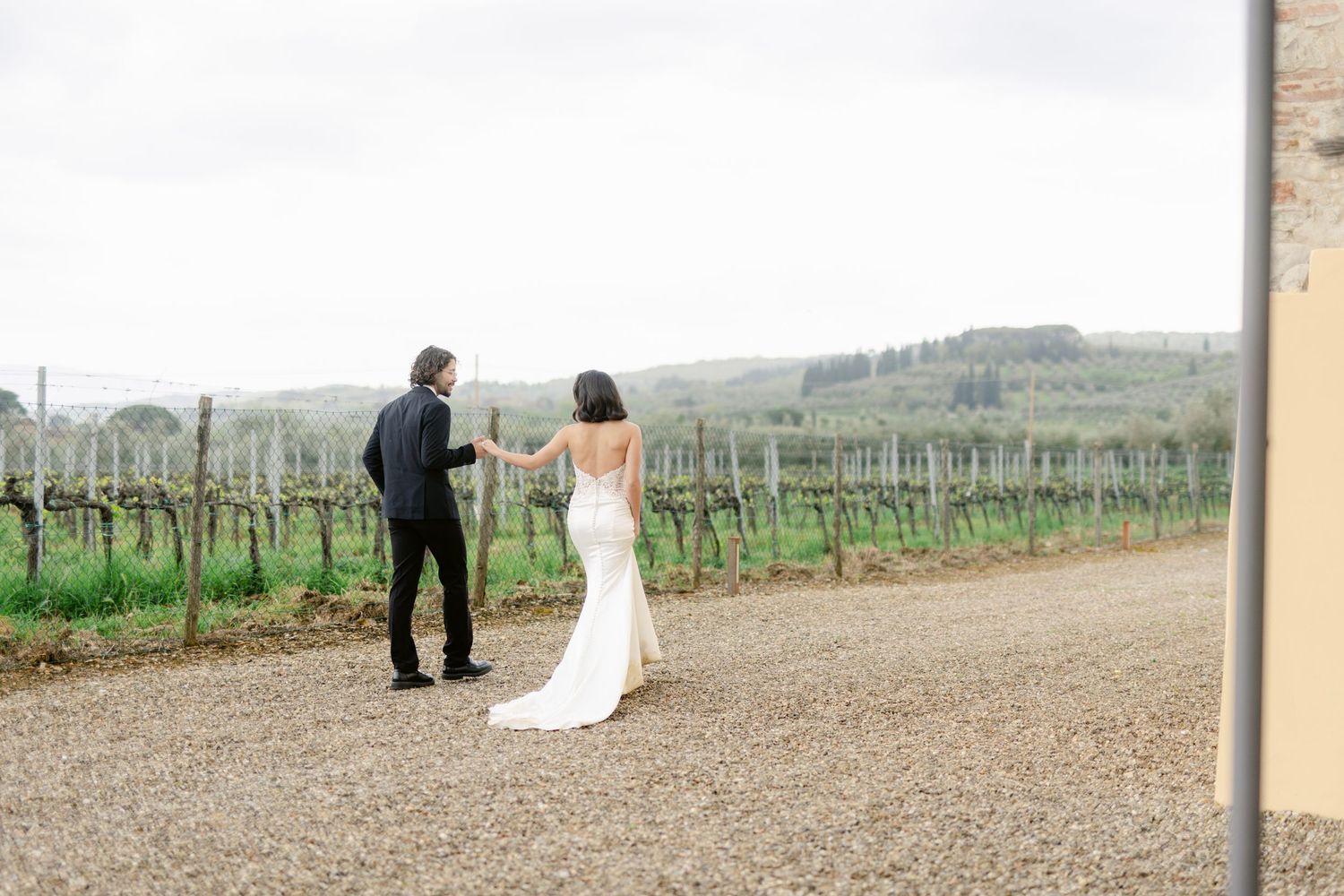 Couple walking along a gravel path beside vineyard rows on an overcast day.