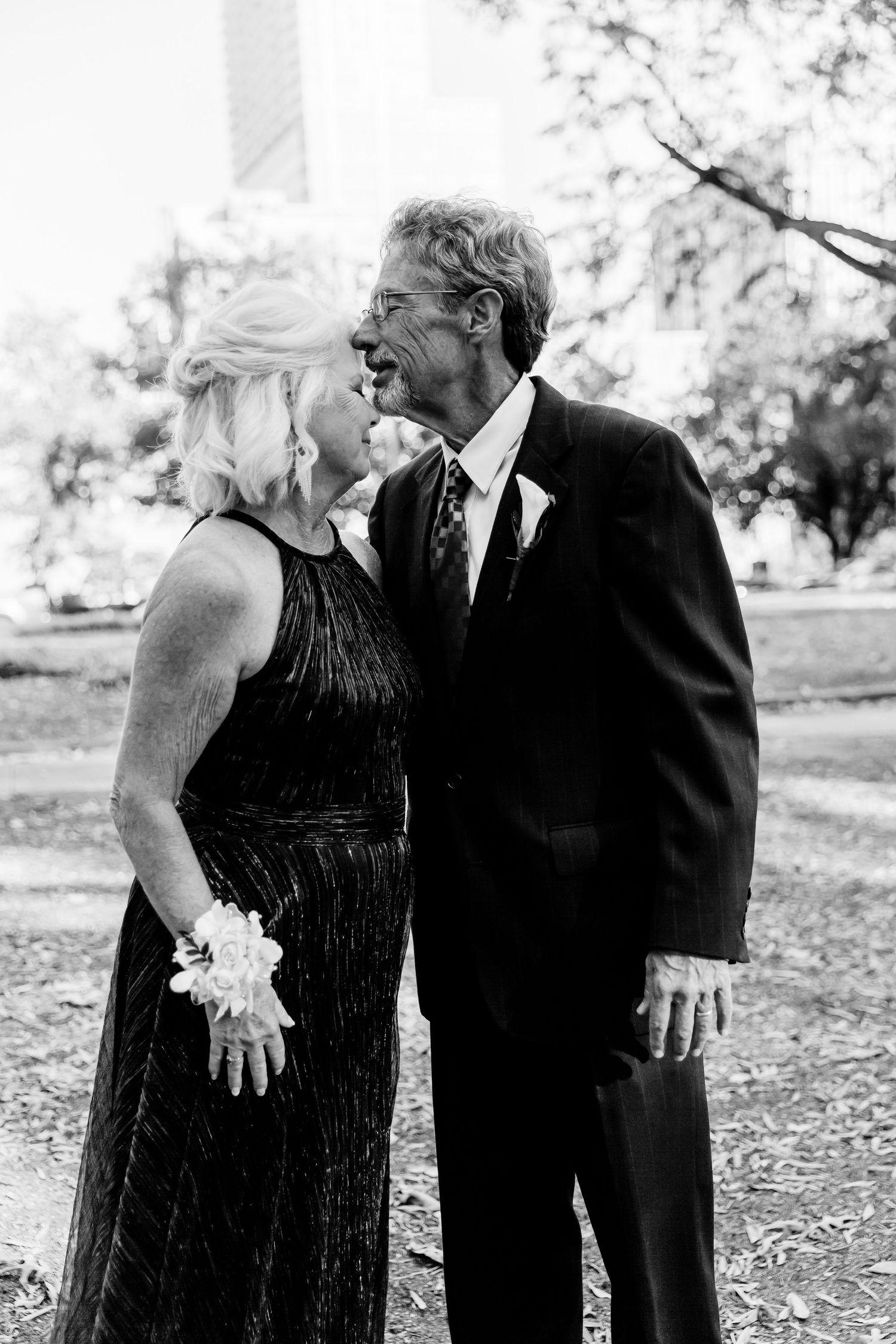 Elegant couple in formal attire share an intimate black and white moment outdoors.