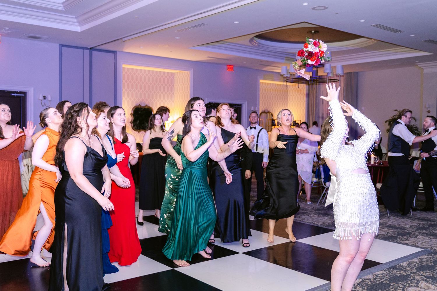 A group of formal dancers in elegant dresses and suits perform choreographed moves at a ballroom event.