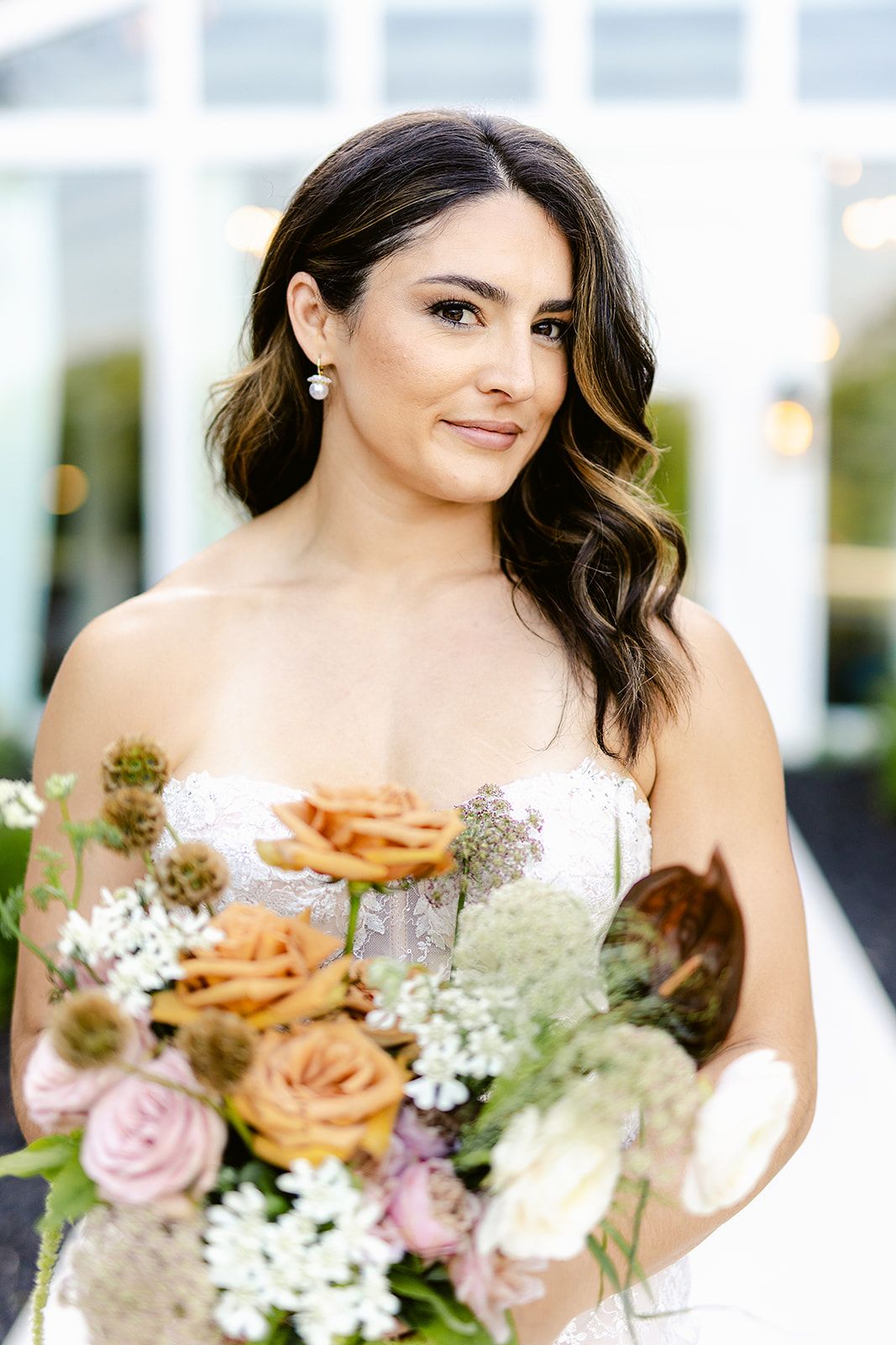 A bride in a white dress holds a romantic bouquet of pink roses, white flowers and dried elements at a wedding.