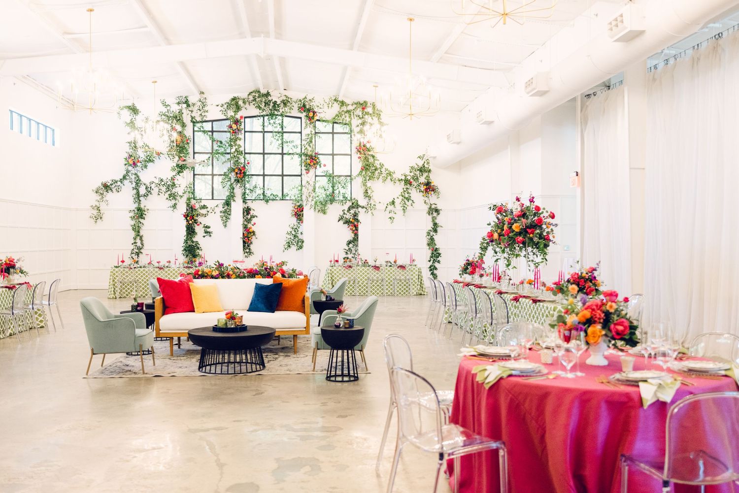 Wedding reception venue decorated with bright floral centerpieces and white drapery in an elegant indoor space.