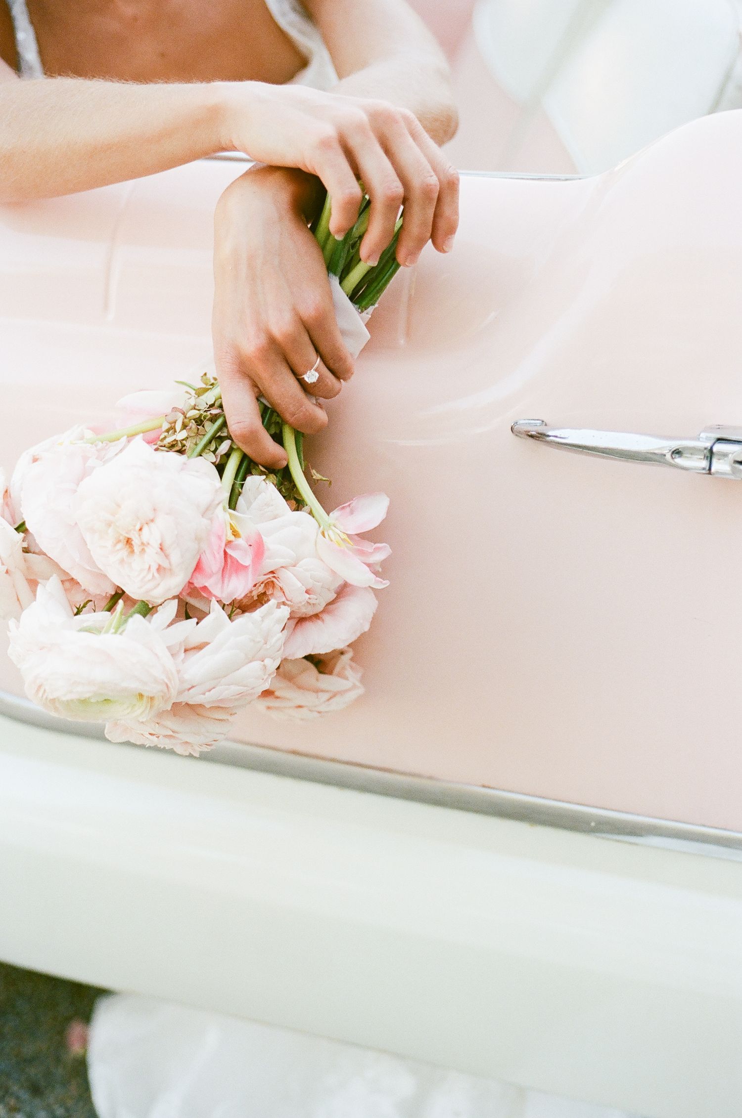 Hands delicately arrange soft pink peonies and flowers on a light pink surface for floral design.