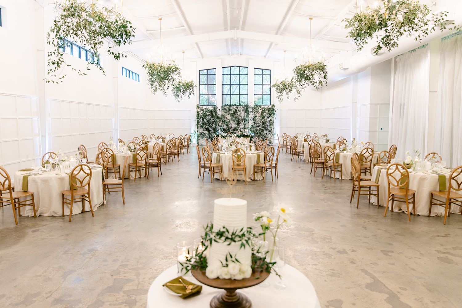 Bright white wedding reception hall with golden chairs and elegant table settings.