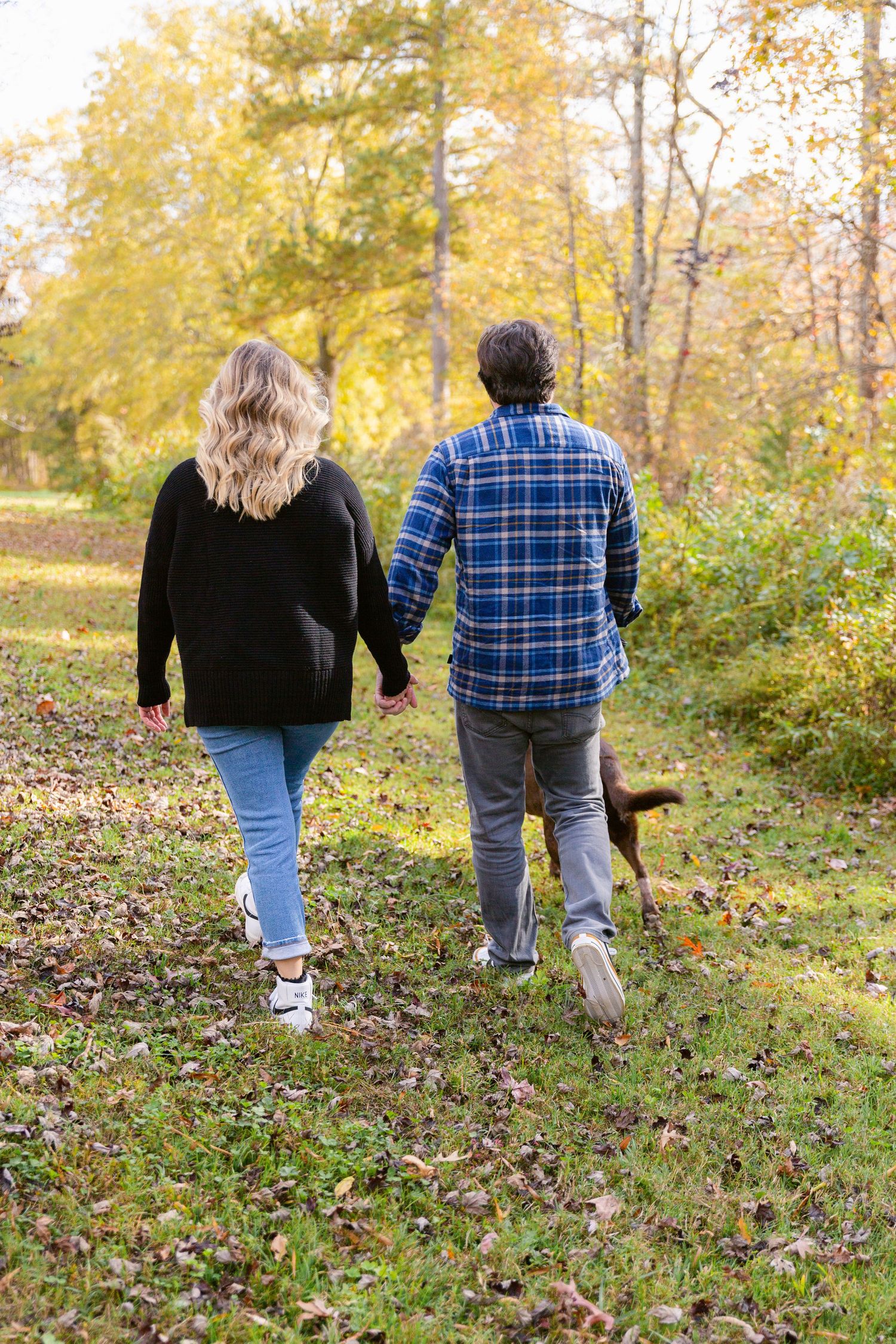 Couple walking hand in hand through autumn woods covered in fallen leaves.