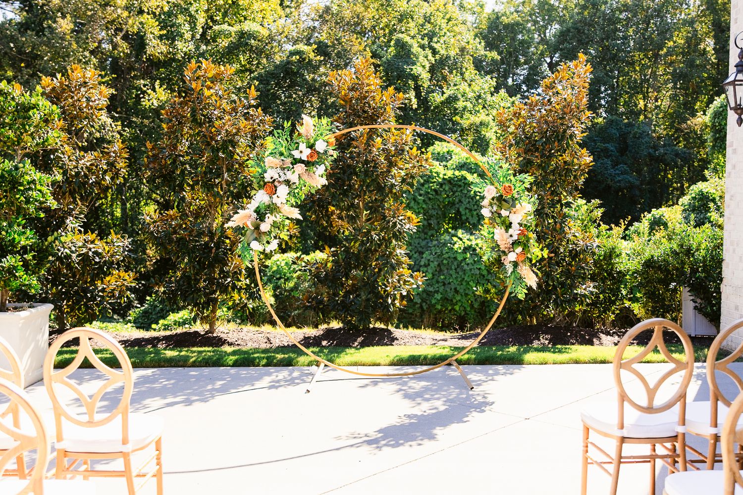 A panoramic view of white wedding chairs arranged in rows outdoors under autumn trees on a sunny day.