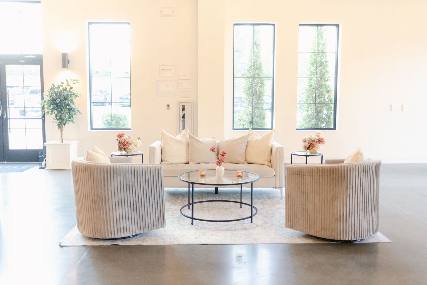 Modern living room setup with beige velvet swivel chairs, round coffee table, and bright windows in a minimalist space.