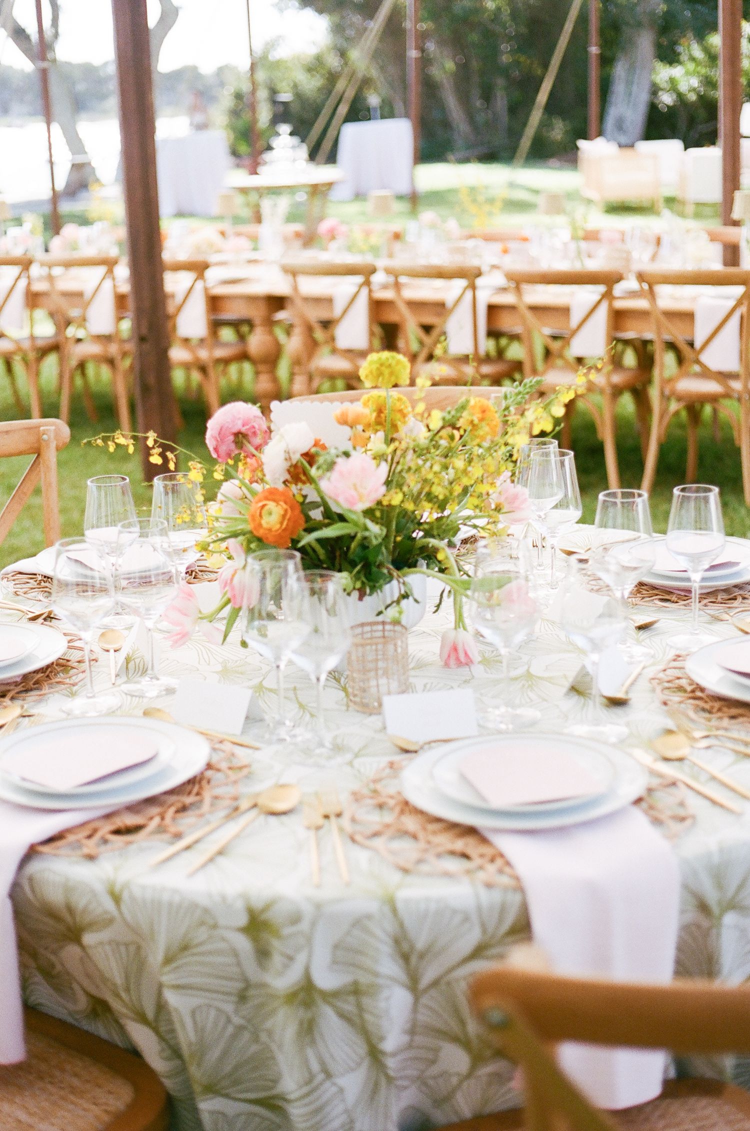 Elegant table setting with colorful floral centerpiece and place settings under tent.