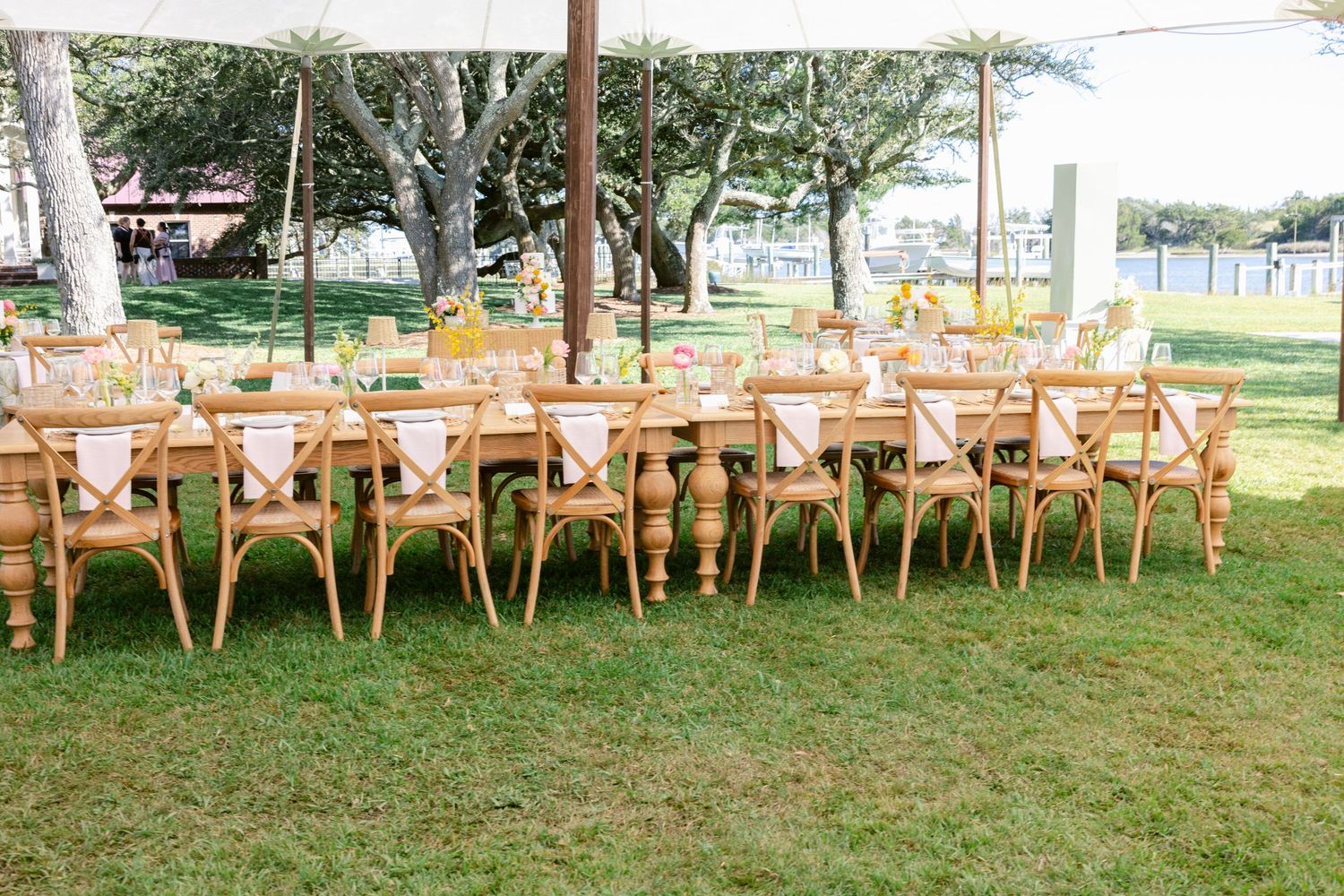 Row of wooden cross-back chairs set up for an outdoor wedding ceremony on green grass.