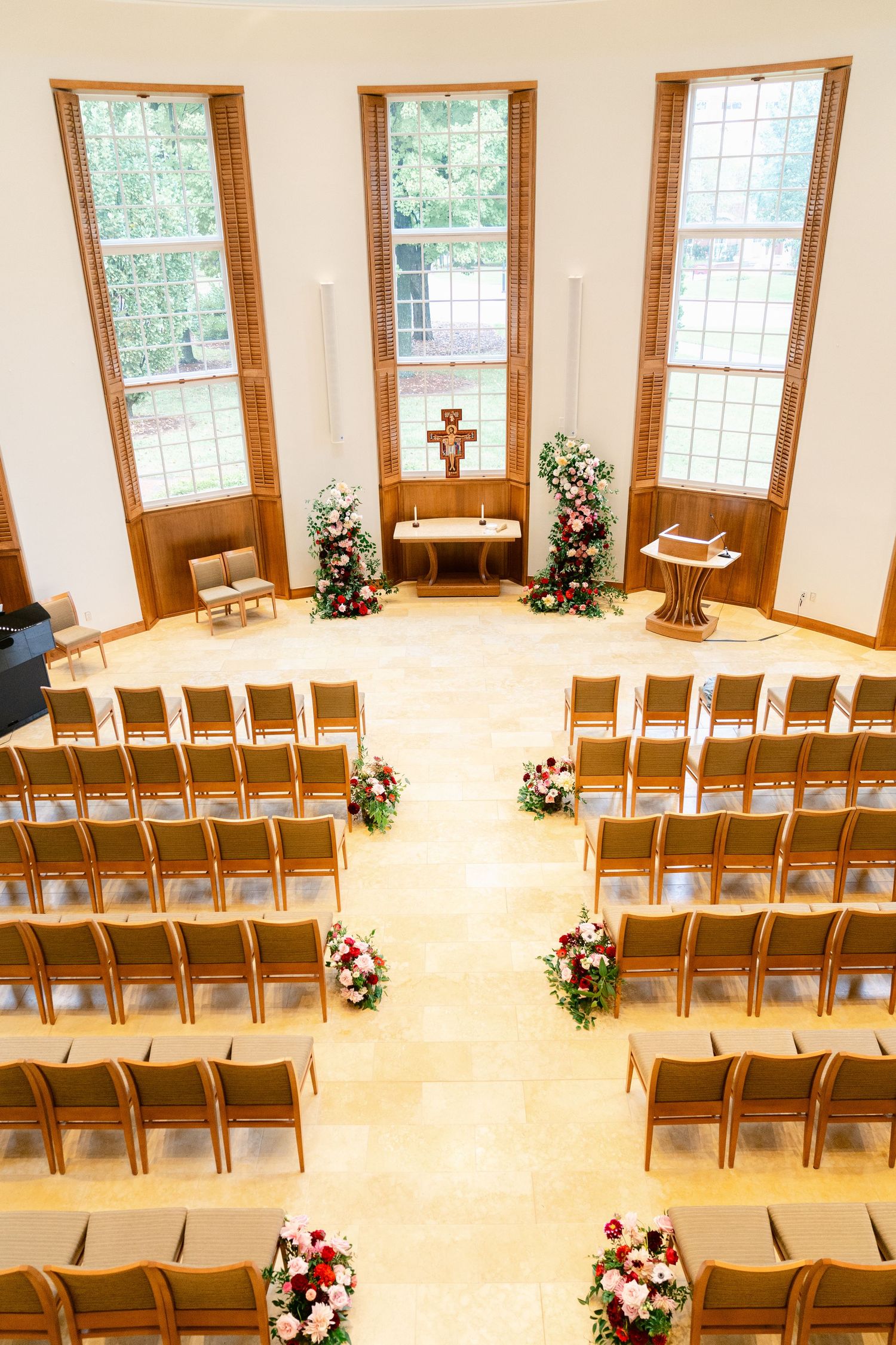 Chapel interior set up for wedding ceremony with wooden chairs and floral arrangements along the aisle.