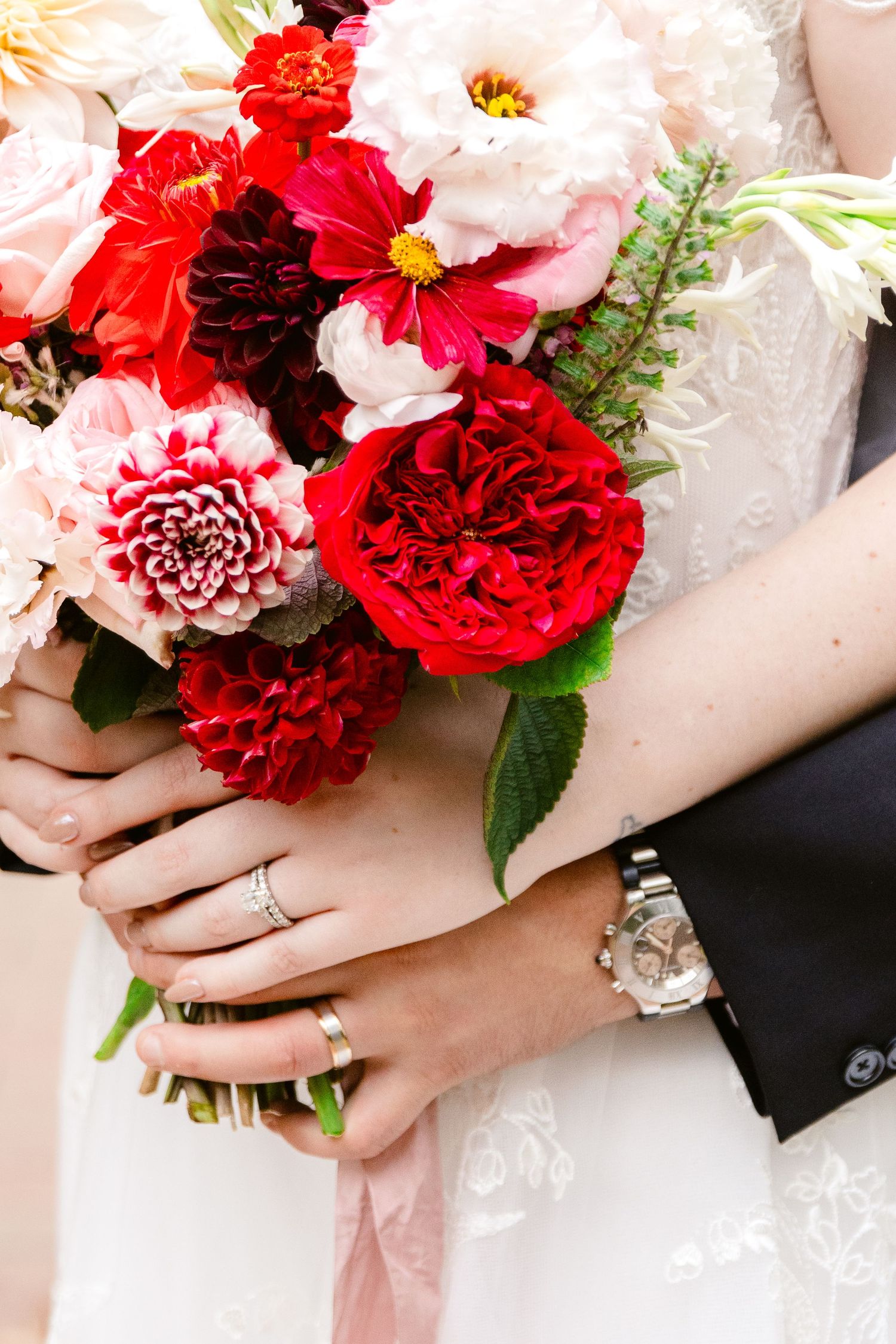 Close-up view of hands holding vibrant red and pink wedding bouquets with roses and mixed flowers.