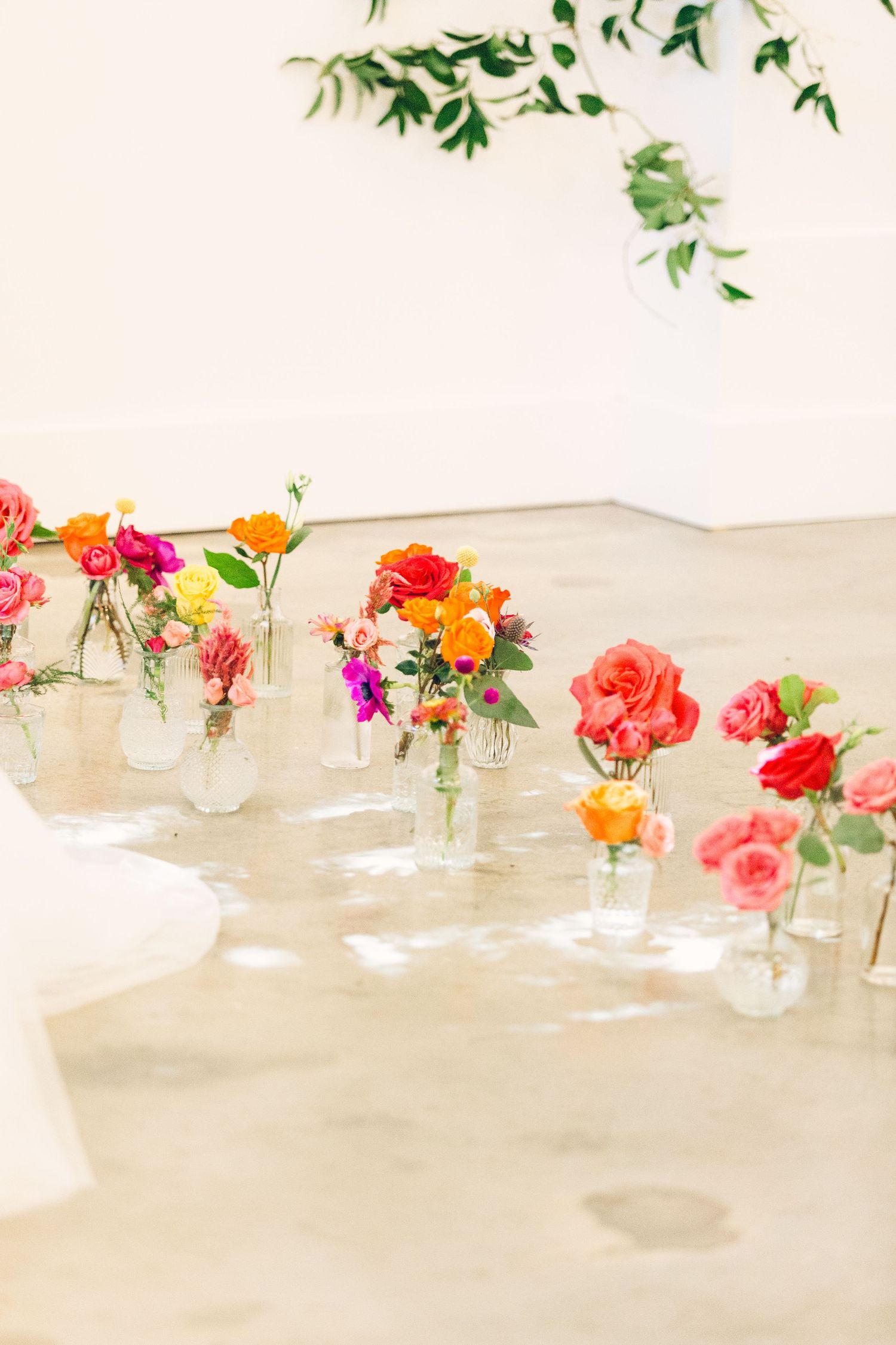 Simple wedding table decor features small glass vases filled with vibrant coral and orange flowers on a white tablecloth.