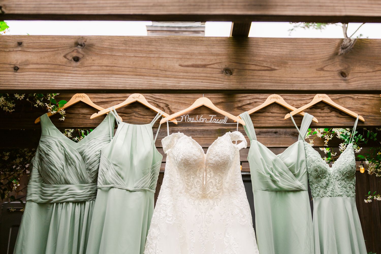 A row of mint green bridesmaid dresses and a white wedding gown hanging on a rustic wooden wall.