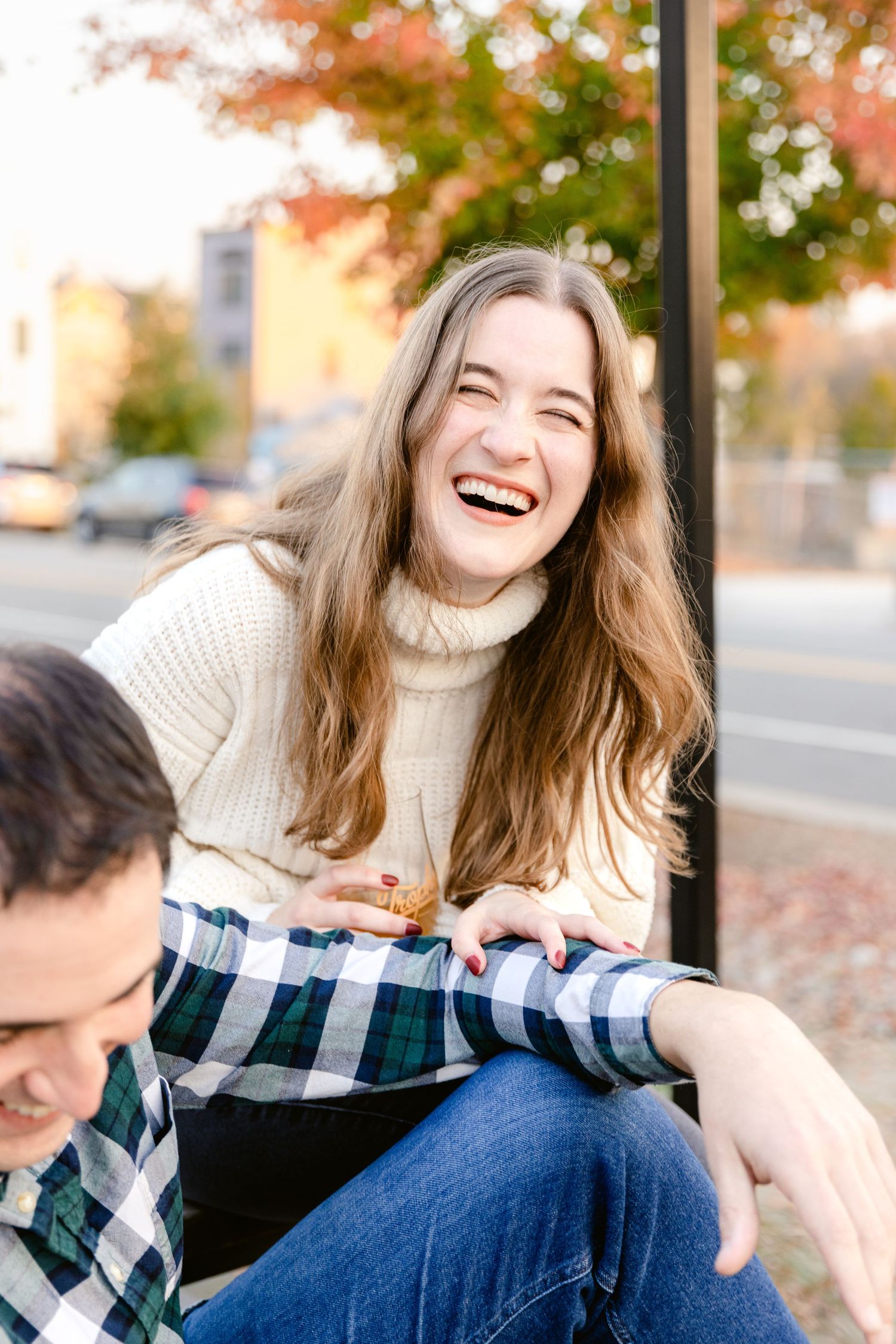 A candid moment of laughter captured outdoors on an autumn day wearing a cream turtleneck sweater.