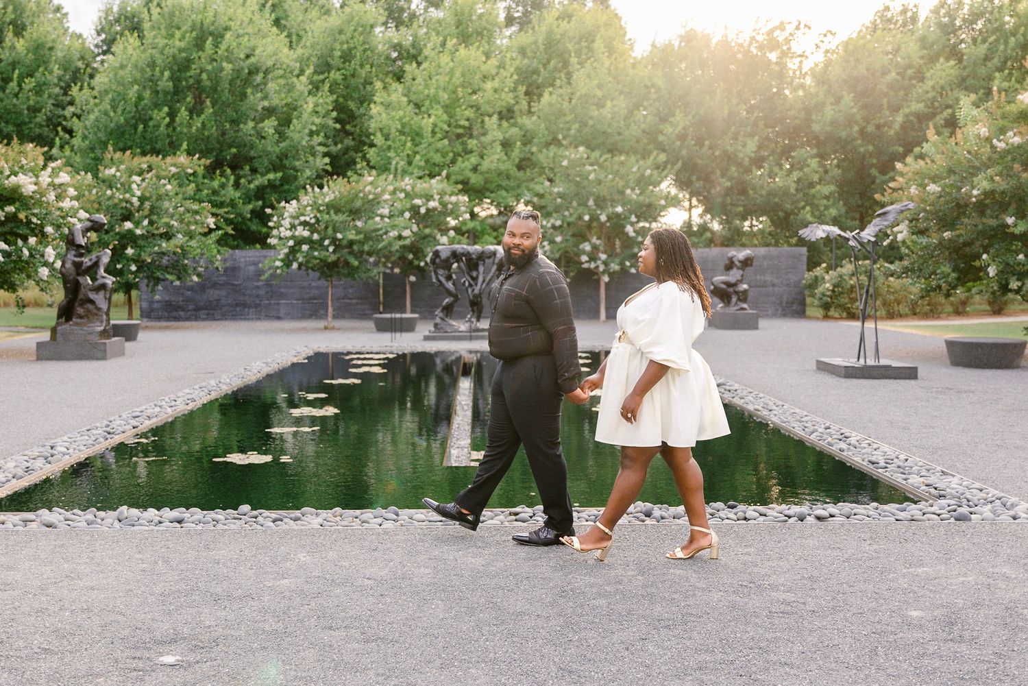 A couple stands together by a reflective pond in a garden setting during golden hour.