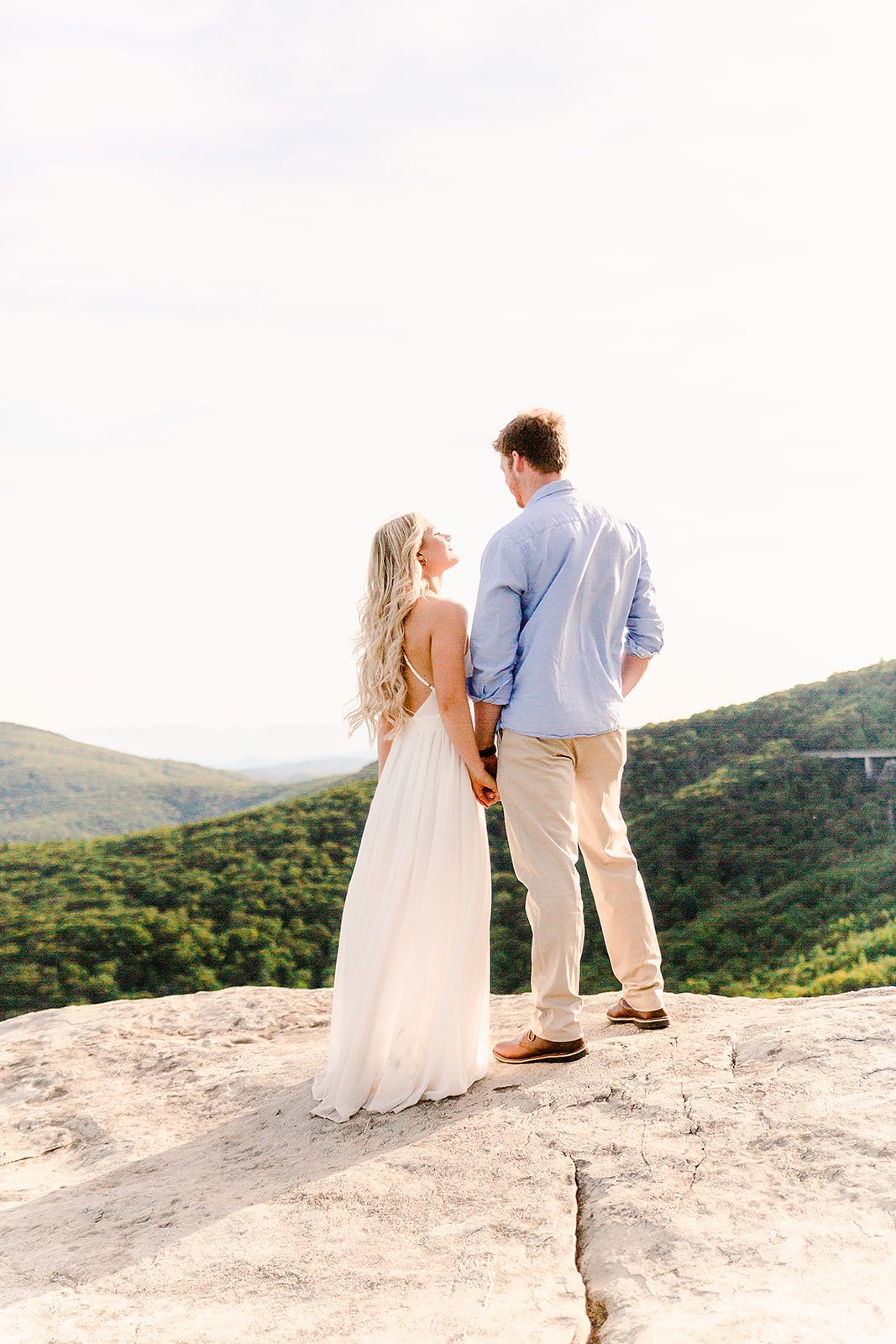 A couple stands together on a scenic mountain overlook surrounded by lush green hills.