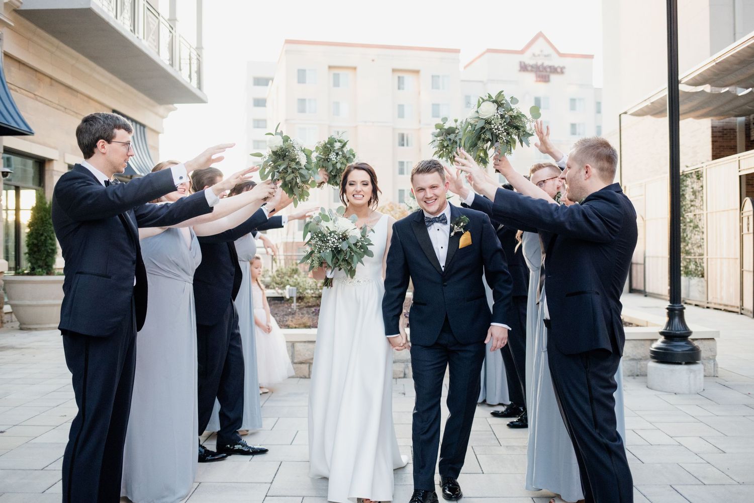 Wedding party creates a tunnel effect with their arms as couple stands in center.