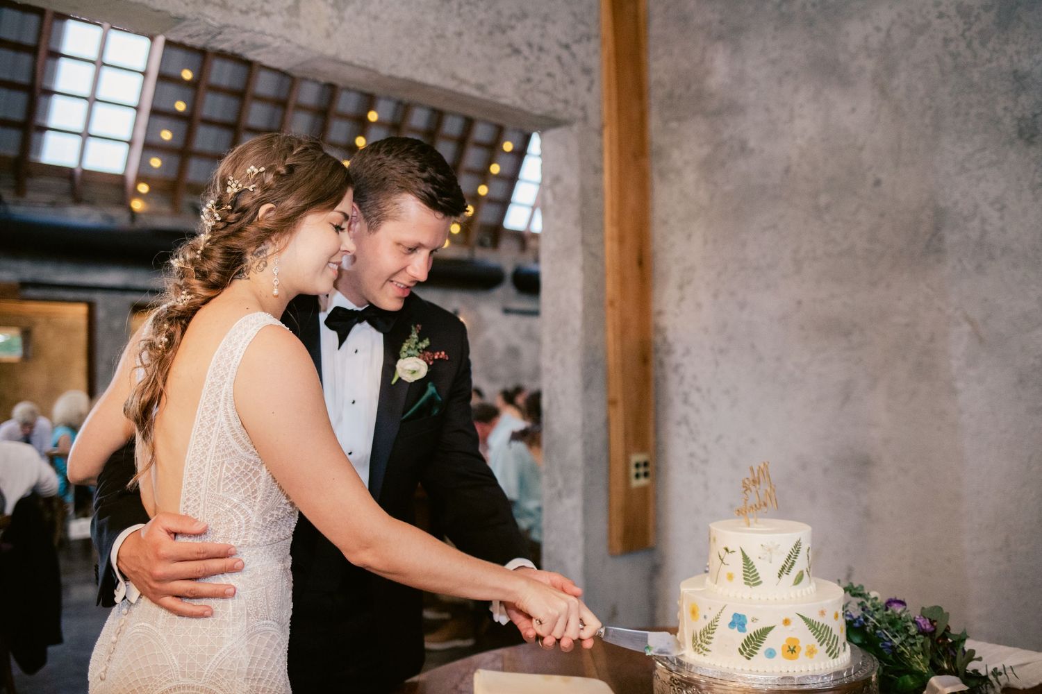 Couple cutting their decorated white wedding cake together at their reception.
