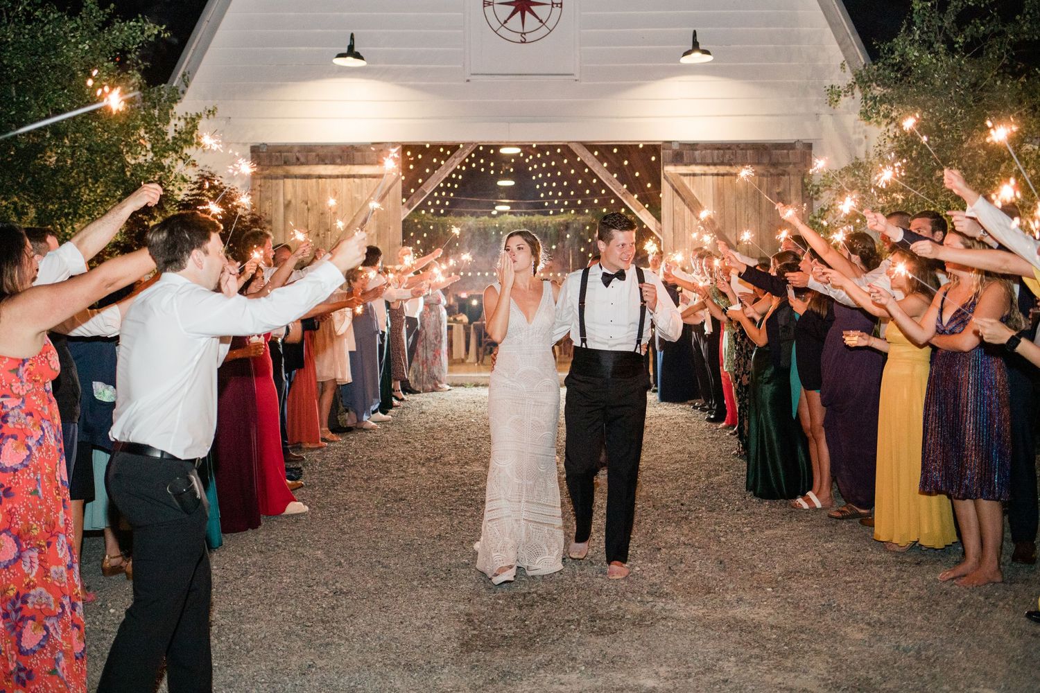 Couple exits wedding venue through sparkler tunnel lined with guests in colorful attire.