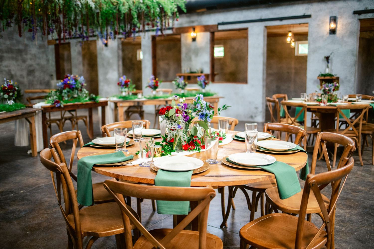 Reception tables set with wooden chairs, green napkins and floral centerpieces.